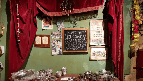 A cozy interior with red drapes, a welcome sign, and various framed photos and calendars on a green wall.