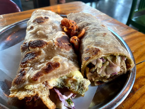 Two stuffed flatbreads on a metal plate, one filled with vegetables and the other with a mix of ingredients, served with snacks.