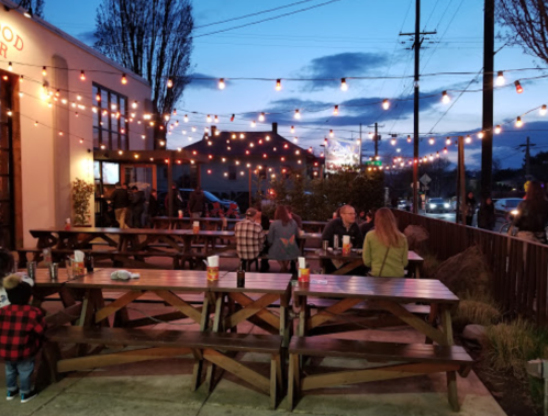Outdoor dining area with wooden tables, string lights, and people enjoying the evening at dusk.