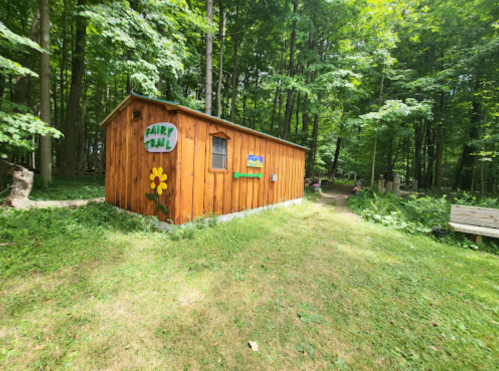 A wooden cabin labeled "Fairy Trail" surrounded by lush green trees and grass in a forest setting.