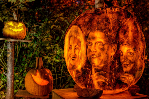 A carved pumpkin featuring three faces, illuminated with a spooky glow, alongside another smiling pumpkin.