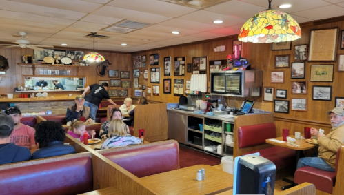 A cozy diner interior with red booths, wooden walls adorned with photos, and patrons enjoying meals.