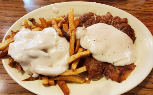 A plate of crispy fries topped with a breaded meat patty smothered in creamy white gravy.