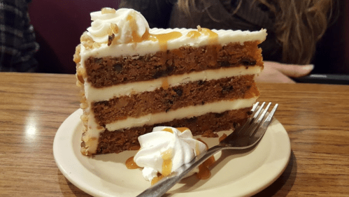 A slice of layered cake with cream frosting, topped with caramel drizzle and a dollop of whipped cream on a plate.