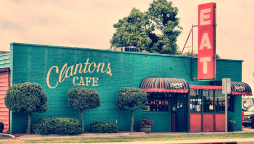 A colorful cafe exterior with "Clanton's Cafe" sign, featuring a large "EAT" sign and trees in front.