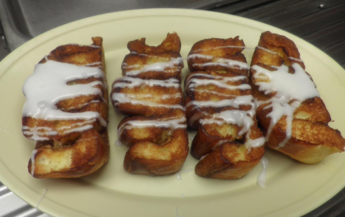 Four pieces of fried dough drizzled with white icing on a yellow plate.