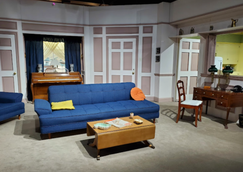 A cozy living room with a blue sofa, wooden furniture, a piano, and decorative accents in a pastel color scheme.