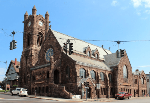 Historic stone church with a tall clock tower, large stained glass window, and surrounding traffic signals.