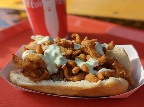A hot dog bun filled with crispy fried shrimp and drizzled with a creamy sauce, served on a red tray.