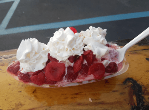 A dessert bowl filled with whipped cream and fresh raspberries on a wooden surface.