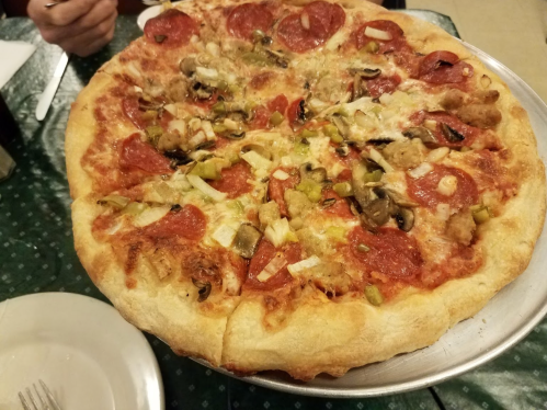 A large pizza topped with pepperoni, mushrooms, green peppers, and onions on a silver serving tray.