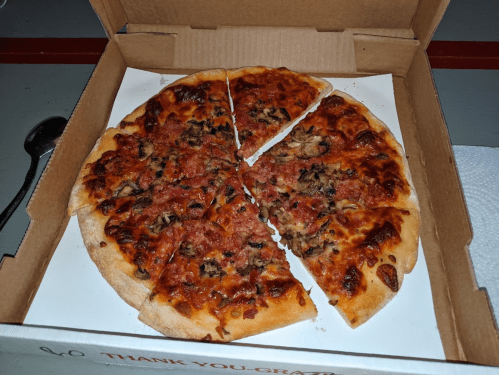 A pizza in a takeout box, sliced into pieces, with toppings of meat and cheese.