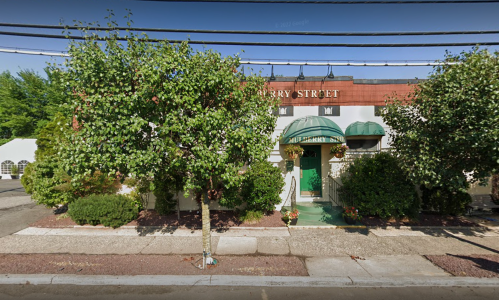 A quaint building with green awnings and trees in front, located on a street with power lines overhead.