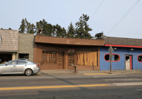 A street view of two buildings, one with brown facade and curtains, the other painted blue with red accents.