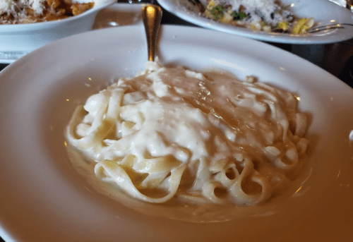 A plate of fettuccine pasta topped with creamy white sauce, served in a white bowl.