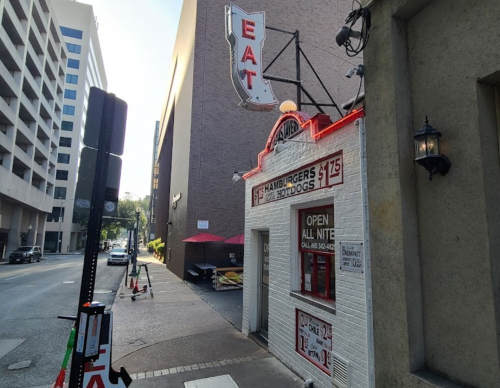 A vintage diner with a neon "EAT" sign, featuring a menu for hamburgers and hot dogs, located on a city street.
