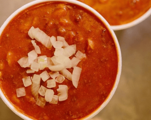 Two bowls of chili topped with chopped onions, showcasing a rich, red sauce.