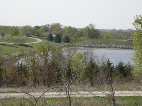 A serene landscape featuring a lake surrounded by greenery and a walking path in the distance.