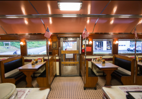 Interior of a diner featuring wooden booths, American flags, and a view of the entrance.