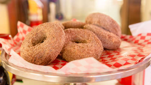 A silver tray holds several cinnamon sugar-coated donuts on red and white checkered paper.
