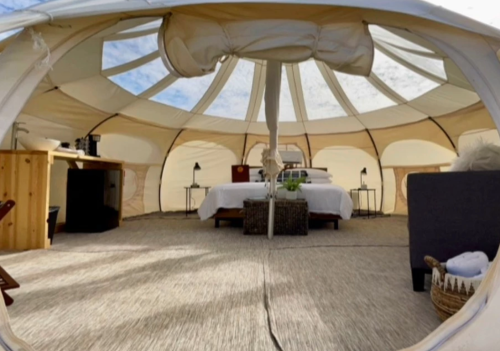 Interior of a spacious, cozy glamping tent with a bed, furniture, and natural light streaming through the top.