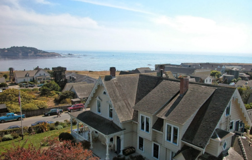 A coastal view featuring a charming house in the foreground and the ocean with distant hills in the background.