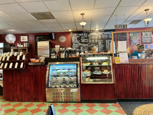 A cozy café interior with a counter, menu board, display case of pastries, and a barista at work.