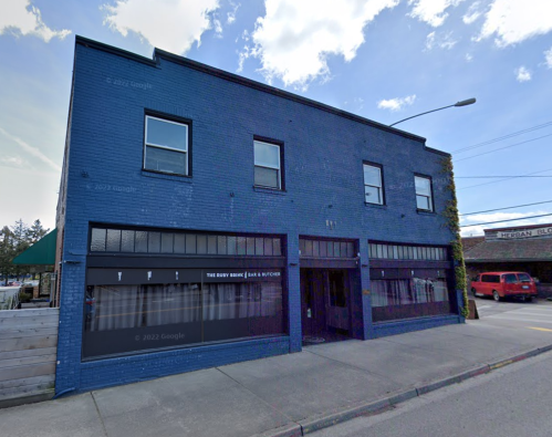 A blue brick building with large windows, featuring a sign for "The Busy Bink Bar & Butcher."
