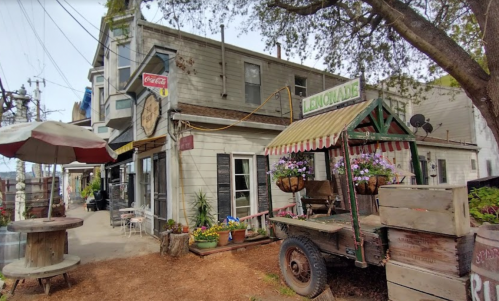 A quaint outdoor scene featuring a lemonade stand, flowers, and a rustic building with a Coca-Cola sign.