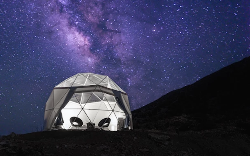A geodesic dome structure under a starry night sky, with the Milky Way visible in the background.