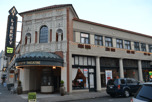 Historic Liberty Theatre building with ornate architecture and marquee, featuring nearby shops and a parked vehicle.