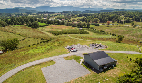 Aerial view of a rural landscape with rolling hills, vineyards, and a small building near a gravel parking area.