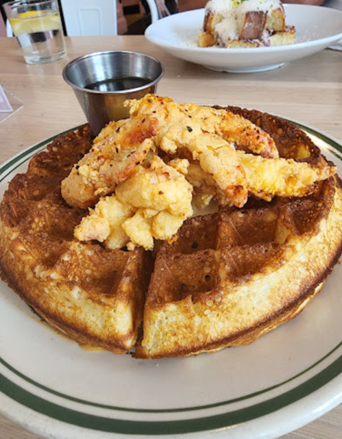 A golden waffle topped with crispy fried chicken and served with a small cup of syrup.