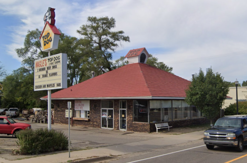 A small, brick fast-food restaurant with a red roof and a sign reading "Top Dog" on a sunny day.