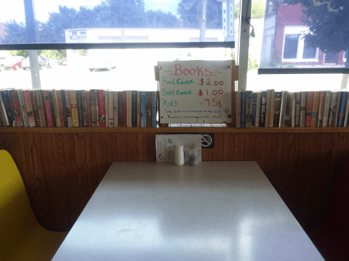 A cozy table in a cafe with a sign about book prices and shelves of books lining the wall.