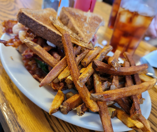 A plate of crispy fries beside a sandwich with bacon and lettuce, served on toasted bread.