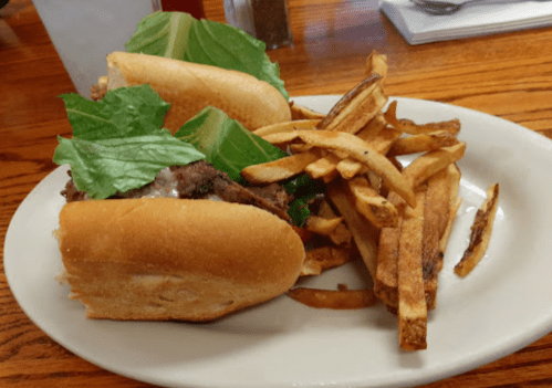 A plate with two sandwiches topped with lettuce and a side of crispy French fries.