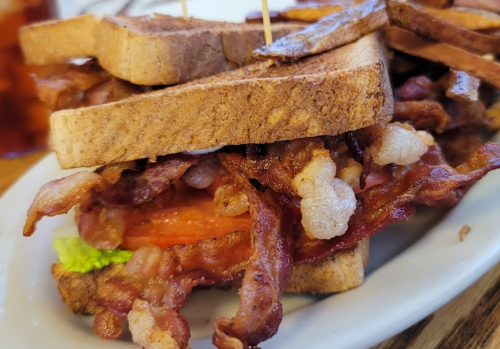 A close-up of a sandwich with layers of crispy bacon, lettuce, and tomato, served with golden-brown fries.