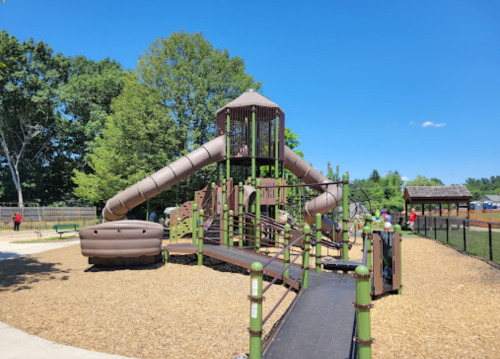 A playground featuring a large slide, climbing structures, and a sandy area under a clear blue sky.