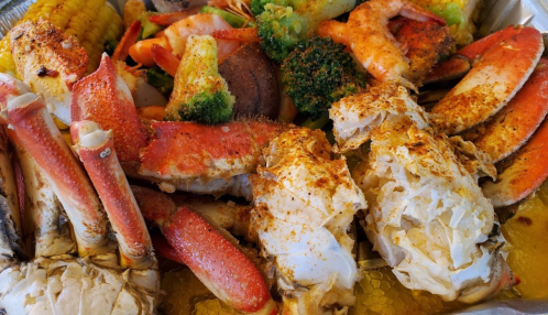 A seafood platter featuring crab legs, shrimp, lobster, corn, and broccoli, seasoned and arranged on a tray.