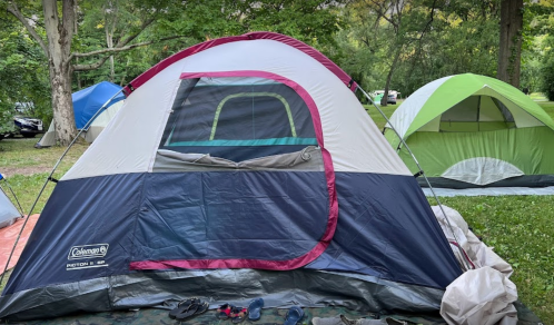 A colorful camping tent set up in a green park, with another tent visible in the background.