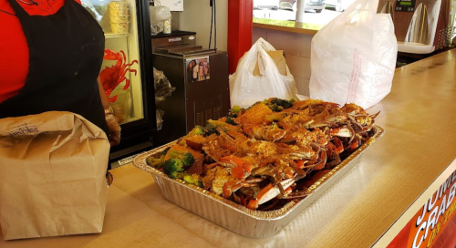 A tray of crabs with broccoli and bread, placed on a counter next to a person in an apron.