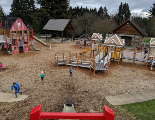 A playground with colorful structures, slides, and children playing on a cloudy day, surrounded by trees.