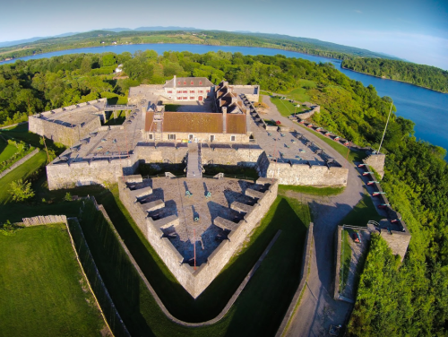 Aerial view of a historic stone fort surrounded by greenery and a river, showcasing its star-shaped layout.