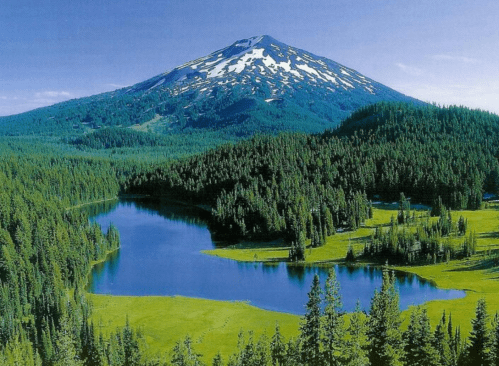 A scenic view of a mountain with snow-capped peaks, surrounded by lush forests and a tranquil lake.