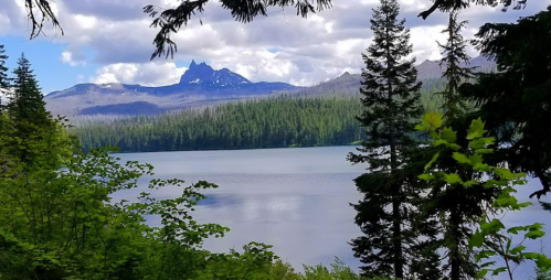 A serene lake surrounded by lush greenery and mountains under a partly cloudy sky.