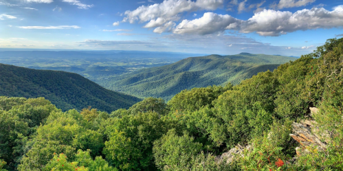 A panoramic view of lush green mountains under a blue sky with scattered clouds.