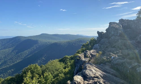 A scenic view of rolling green mountains under a clear blue sky, with rocky outcrops in the foreground.