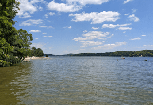 A serene lake scene with clear blue skies, fluffy clouds, and lush greenery along the shore.