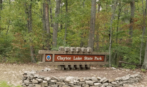 Sign for Clayton Lake State Park surrounded by trees and a stone border.